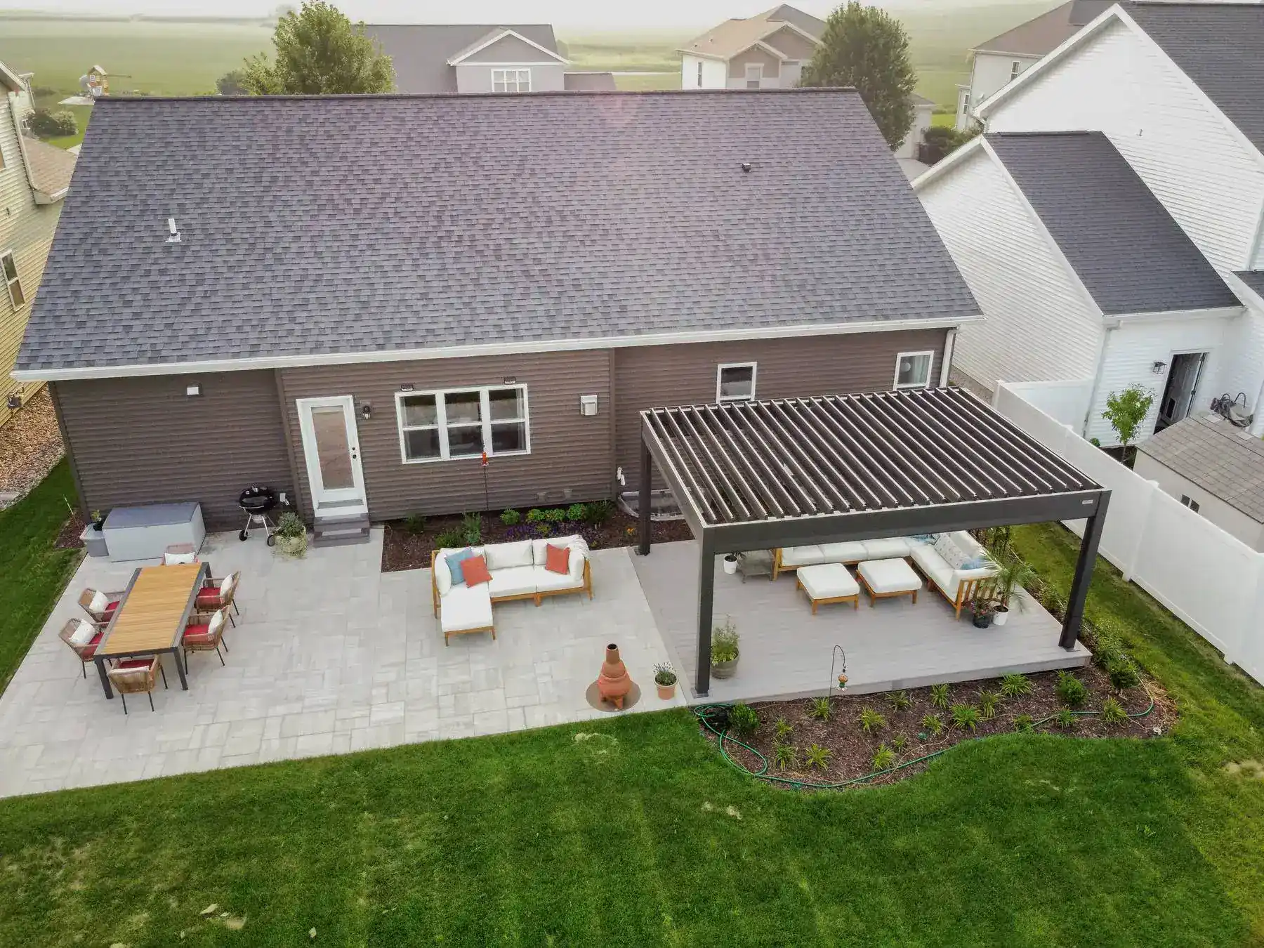 Aerial view of a home with an attached patio and a ground level deck covered with a louvered pergola in slinger wi