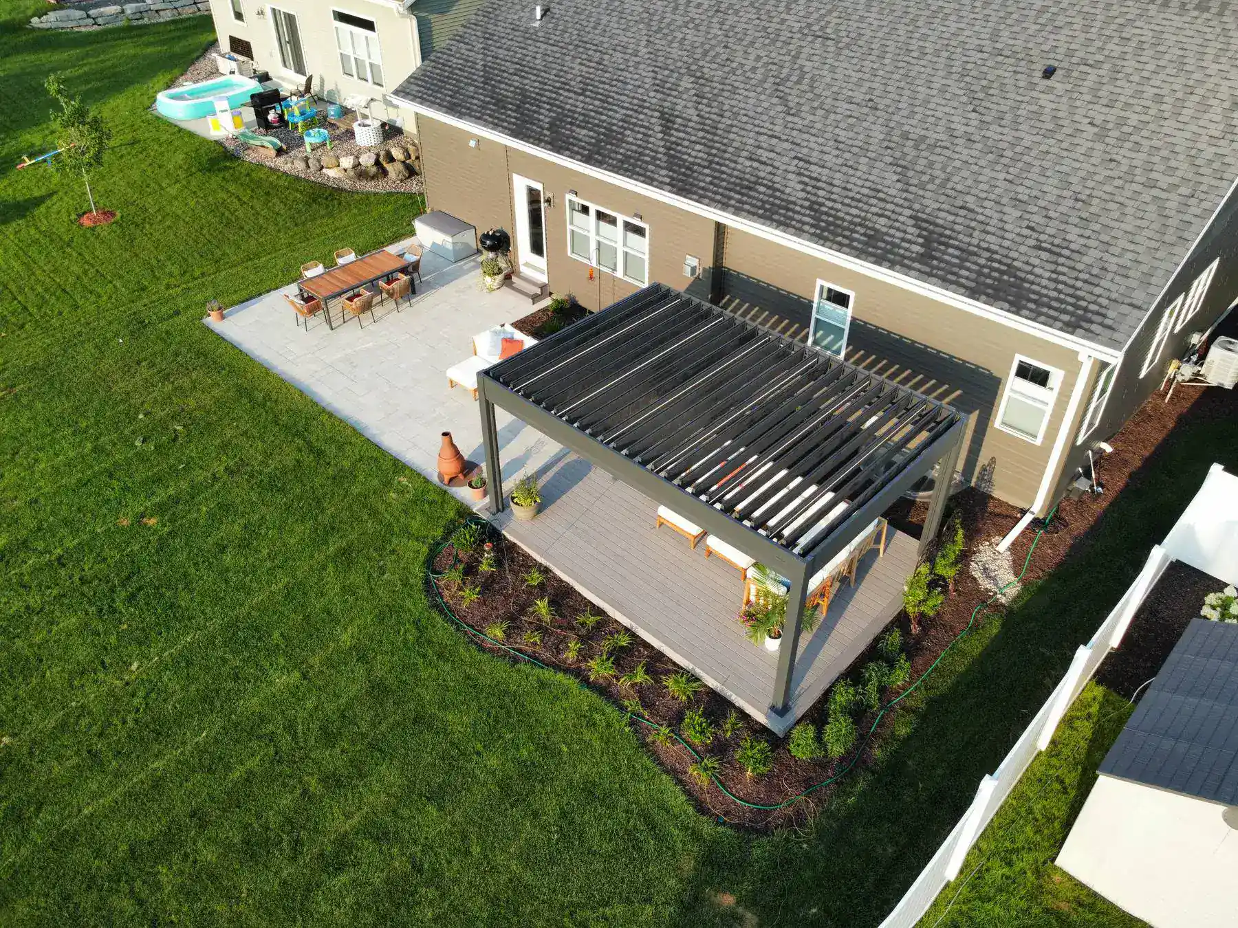 Aerial view of the attached ground level deck with louvered pergola with outdoor living spaces in slinger wi